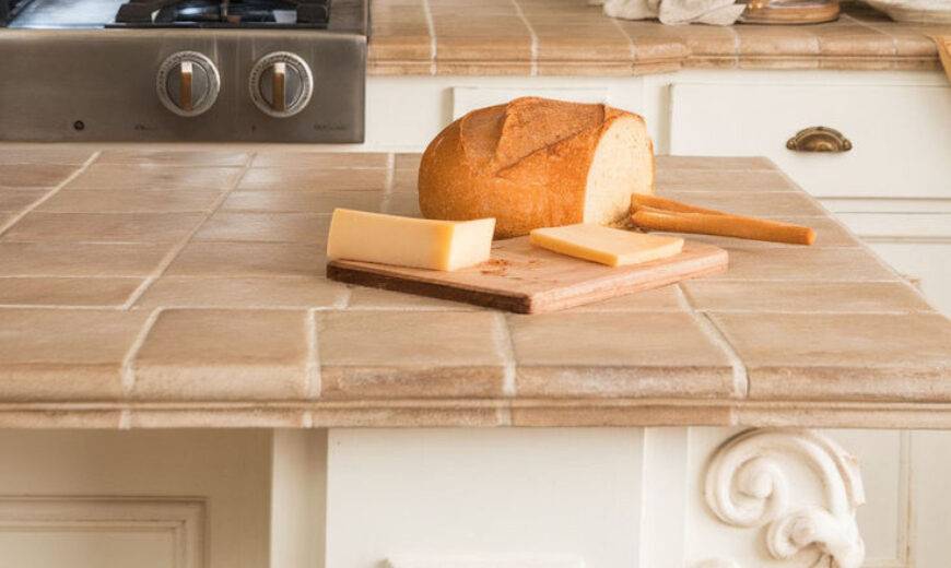 A close photo of a kitchen island with a tile countertop, a loaf of bread on a cutting board on top.