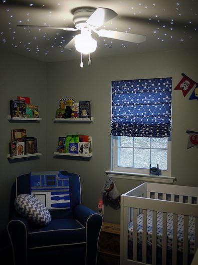 Space nursery with lights on the ceiling, a white crib, and a blue chair flanked by floating shelves.