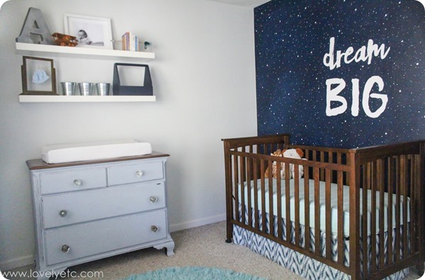Space nursery with a dark wood crib and a star-themed wallpaper with the words "dream BIG"
