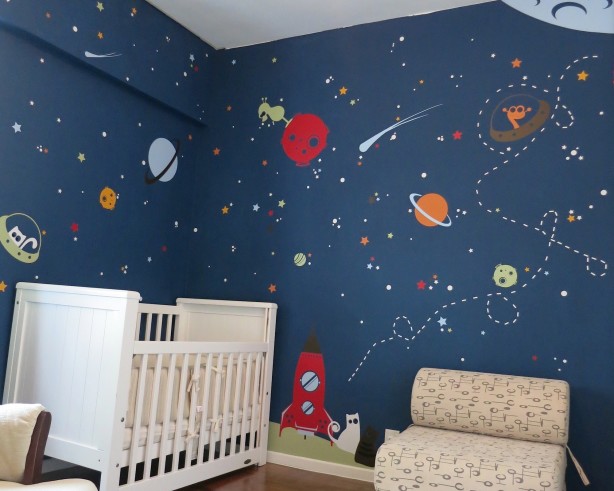 Space nursery with a cartoon-like space theme and a white crib beside a chair with a low back.